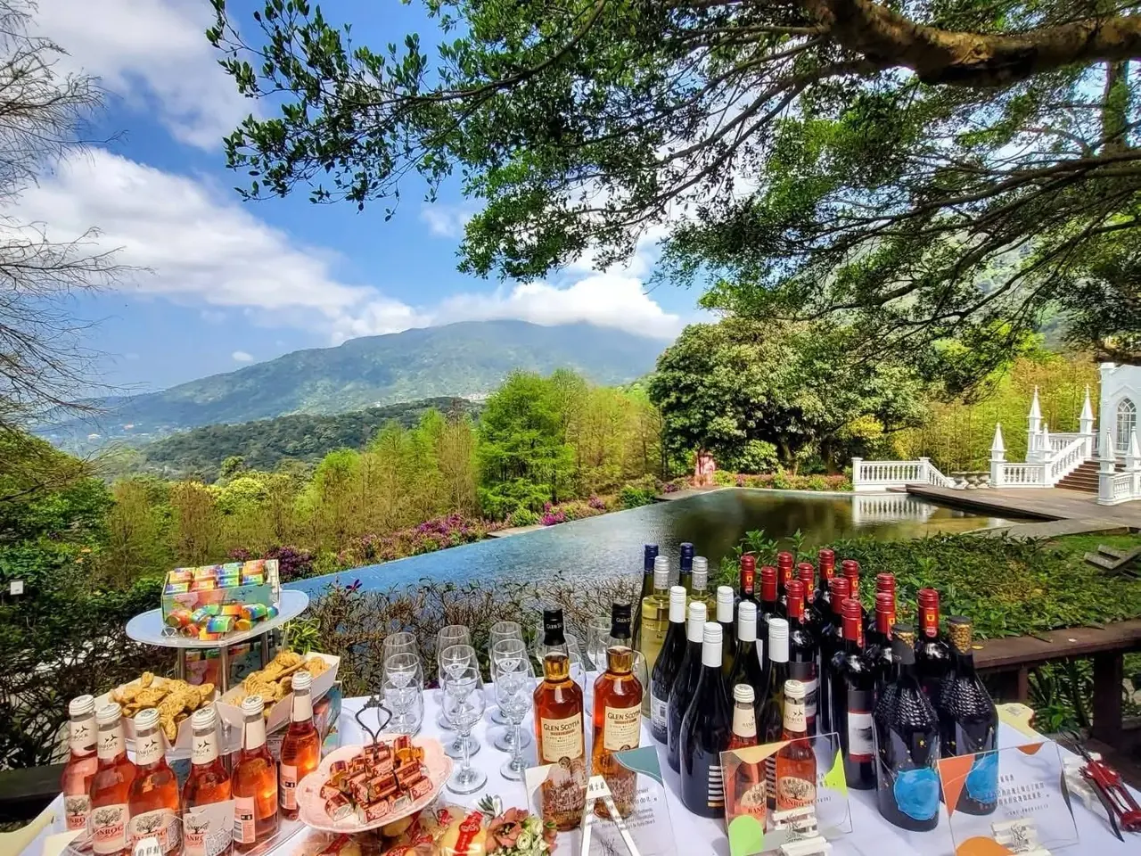 甜點酒水檯 真愛桃花源戶外甜點與酒水檯,長桌陳列各式葡萄酒、氣泡酒與手工甜點,背景為老樹樹冠與陽明山湖景