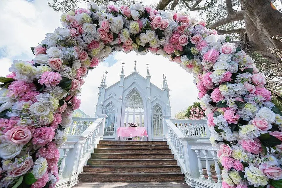 花拱門・教堂 真愛桃花源粉白玫瑰花拱門,透過花圈框出白色哥德式教堂與階梯步道,是證婚儀式入場與合影的主要位置