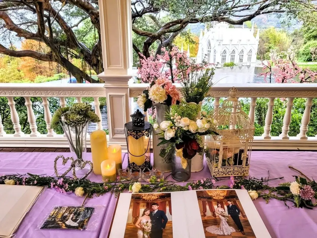 簽名桌 真愛桃花源婚宴簽名桌,桌面陳列新人合照、花藝與燭台,欄杆外即為白色哥德式教堂與庭園