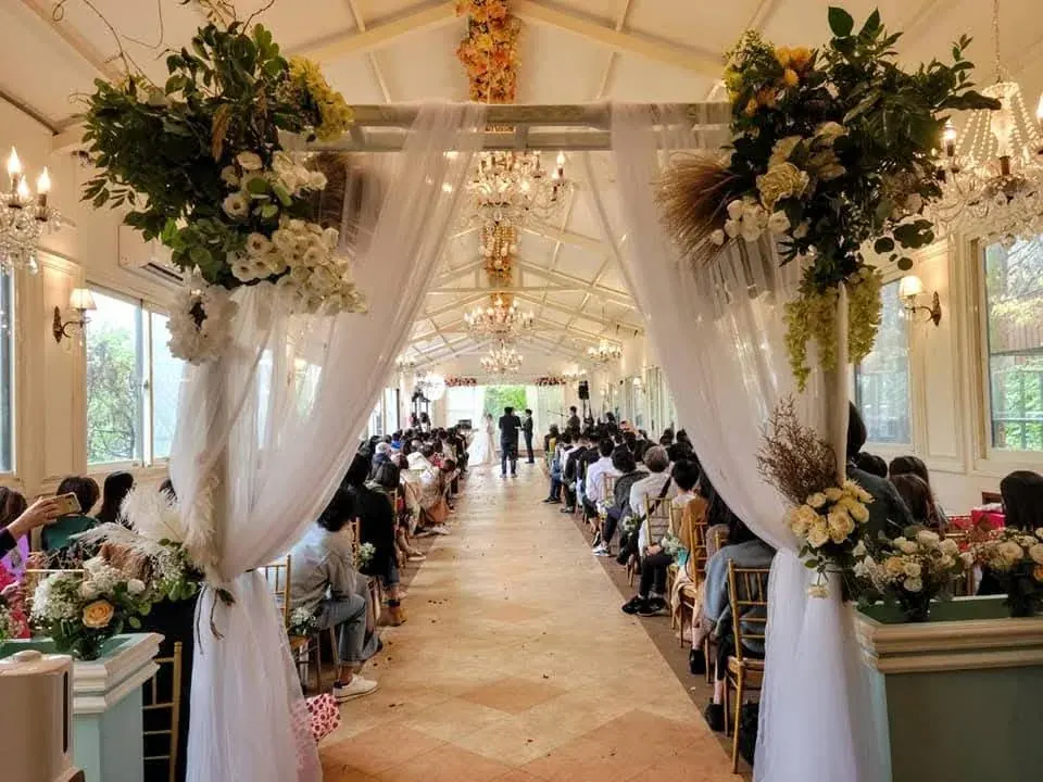 室內證婚 真愛桃花源室內婚禮儀式,白紗與大型花藝裝飾入口拱門,紅毯兩側賓客就座,水晶吊燈與挑高白色屋架構成典禮空間