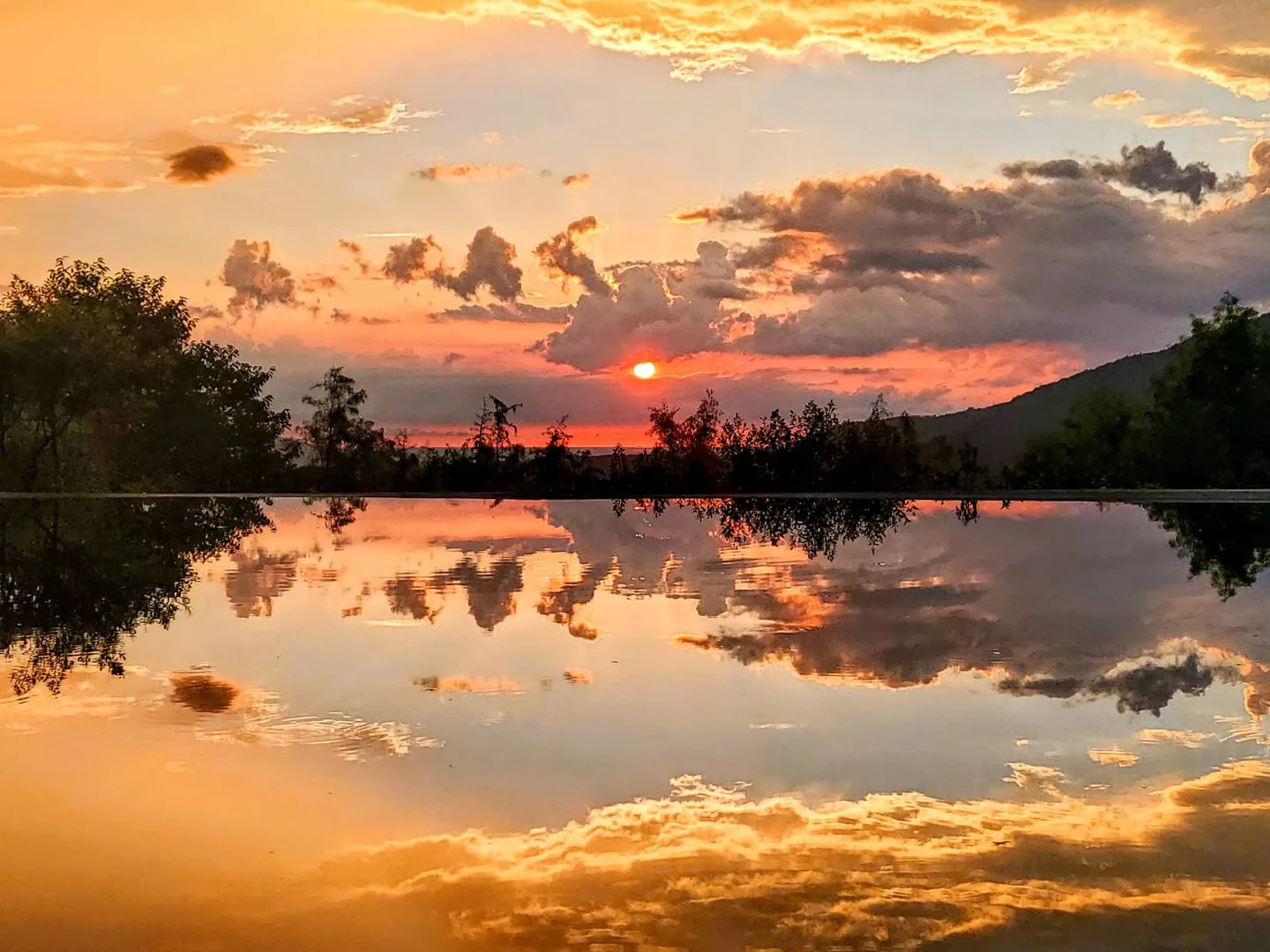 真愛桃花源湖面完整倒映橘紅色夕陽與雲霞，遠處為陽明山稜線剪影