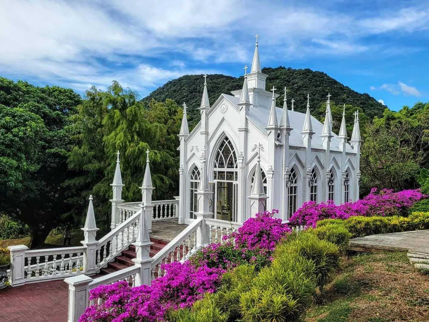 教堂杜鵑季 真愛桃花源哥德式教堂春季實景,白色尖塔建築前方杜鵑盛開成桃紅花帶,白石欄杆階梯通往教堂正門